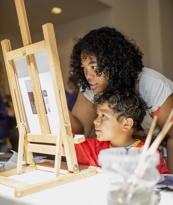 Een kind doet een workshop in de Kunstwerkplaats in het Mauritshuis, zijn moeder kijkt mee.