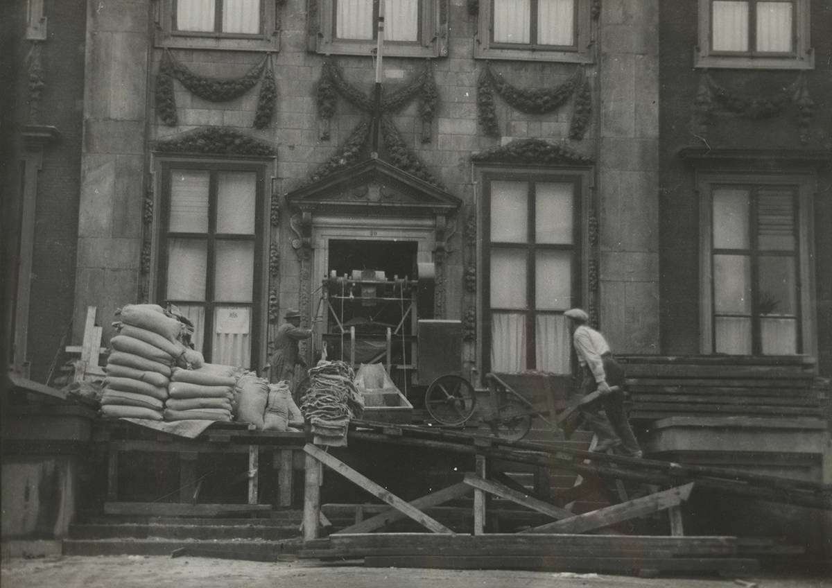 Bouw van de ondergrondse kunstkluis in het Mauritshuis. Er staat een installatie voor het Mauritshuis. Een man met een kruiwagen loopt via een ramp naar boven. Een andere man takelt iets naar binnen.