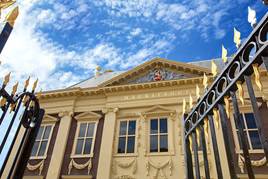 Het Mauritshuis, gezien vanaf de poorten van het voorplein. Je ziet nog een klein stukje hek met sierlijke, gouden punten. 