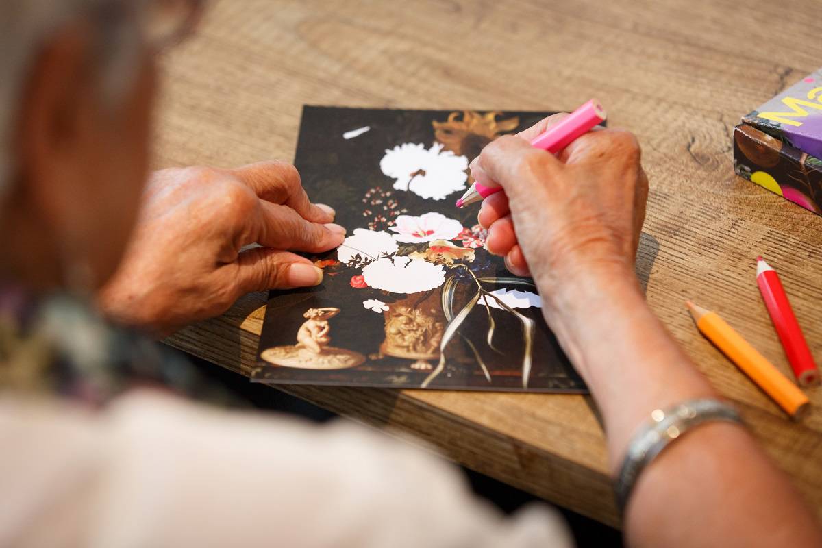Een kleurplaat van een bloemstilleven wordt door een oudere vrouw ingekleurd.