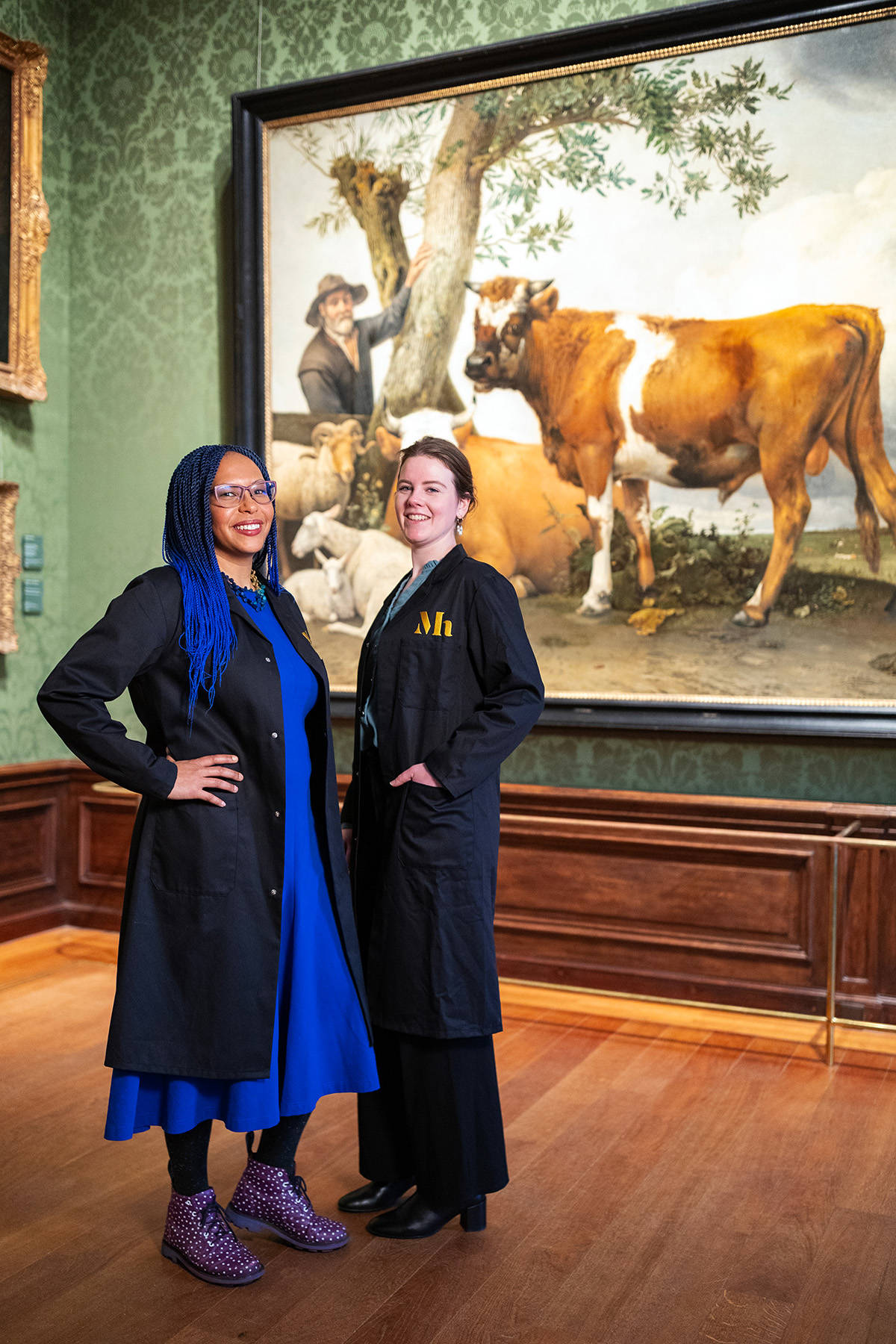 Potterkijkers Abbie En Jolijn staan voor het werk De Stier van Paulus Potter en kijken in de camera.