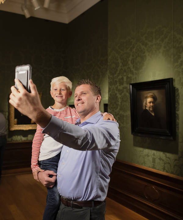 Een vader en zoon maken een selfie bij een zelfportret van Rembrandt in het Mauritshuis in Den Haag.