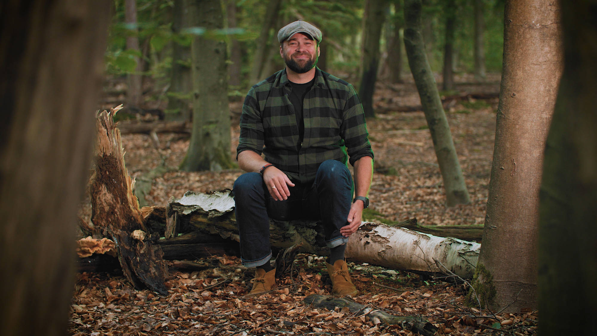 Boswachter Tim zit guitig op een boomstam in het bos.