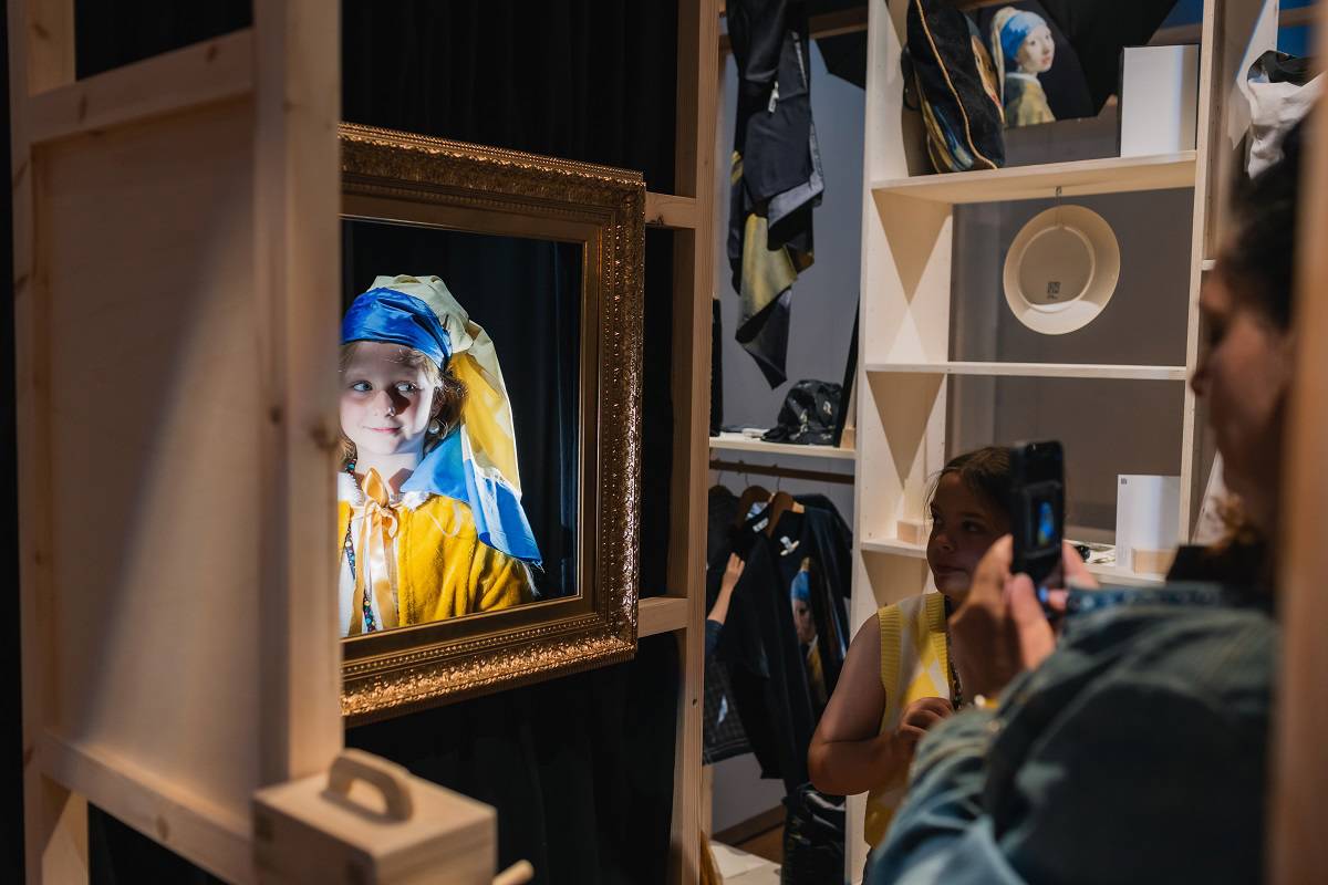 Een meisje verkleed als Het Meisje met de Parel poseert in een gouden lijst. Een bezoeker maakt een foto.