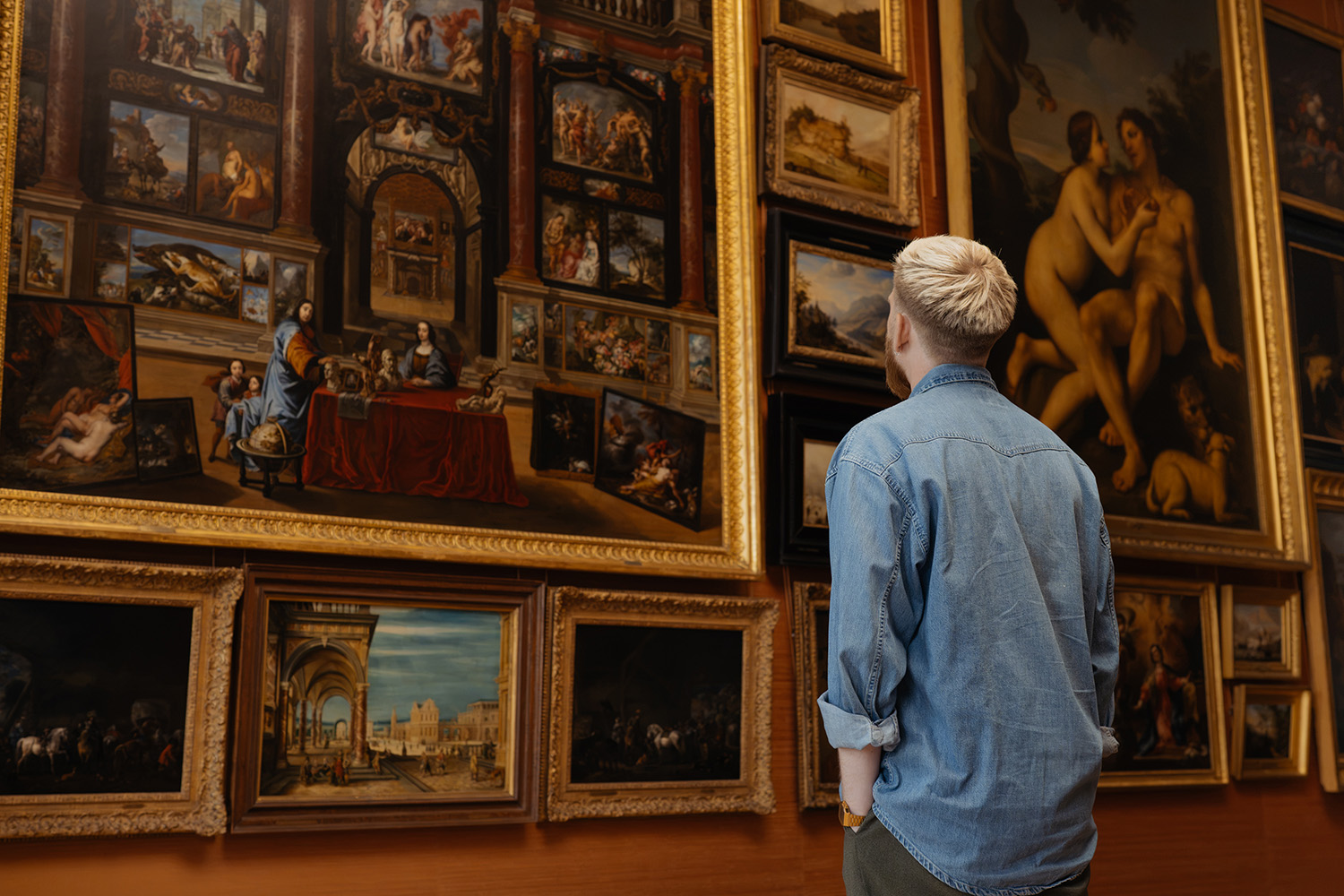 Een bezoeker kijkt naar een muur vol schilderijen in Galerij Prins Willem V.