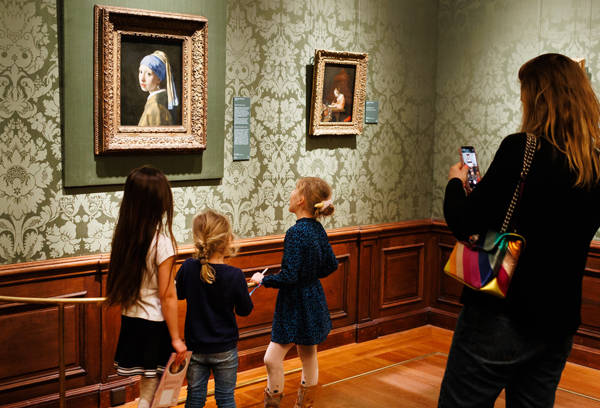Een volwassen vrouw fotografeert kinderen bij Vermeer's Meisje met de Parel.