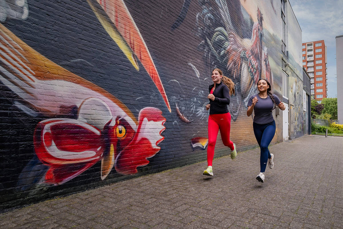 Twee vrouwen rennen langs één van de Mauritshuis Murals in Den Haag.