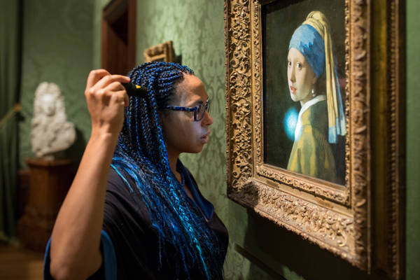 Restaurator Abbie Vandivere schijnt met een lamp op 'Meisje met de parel' van Johannes Vermeer