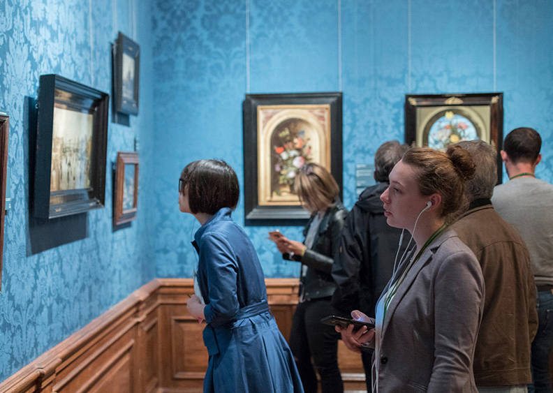 Bezoekers bekijken schilderijen in het Mauritshuis. Eén vrouw maakt gebruik van de multimediatour.