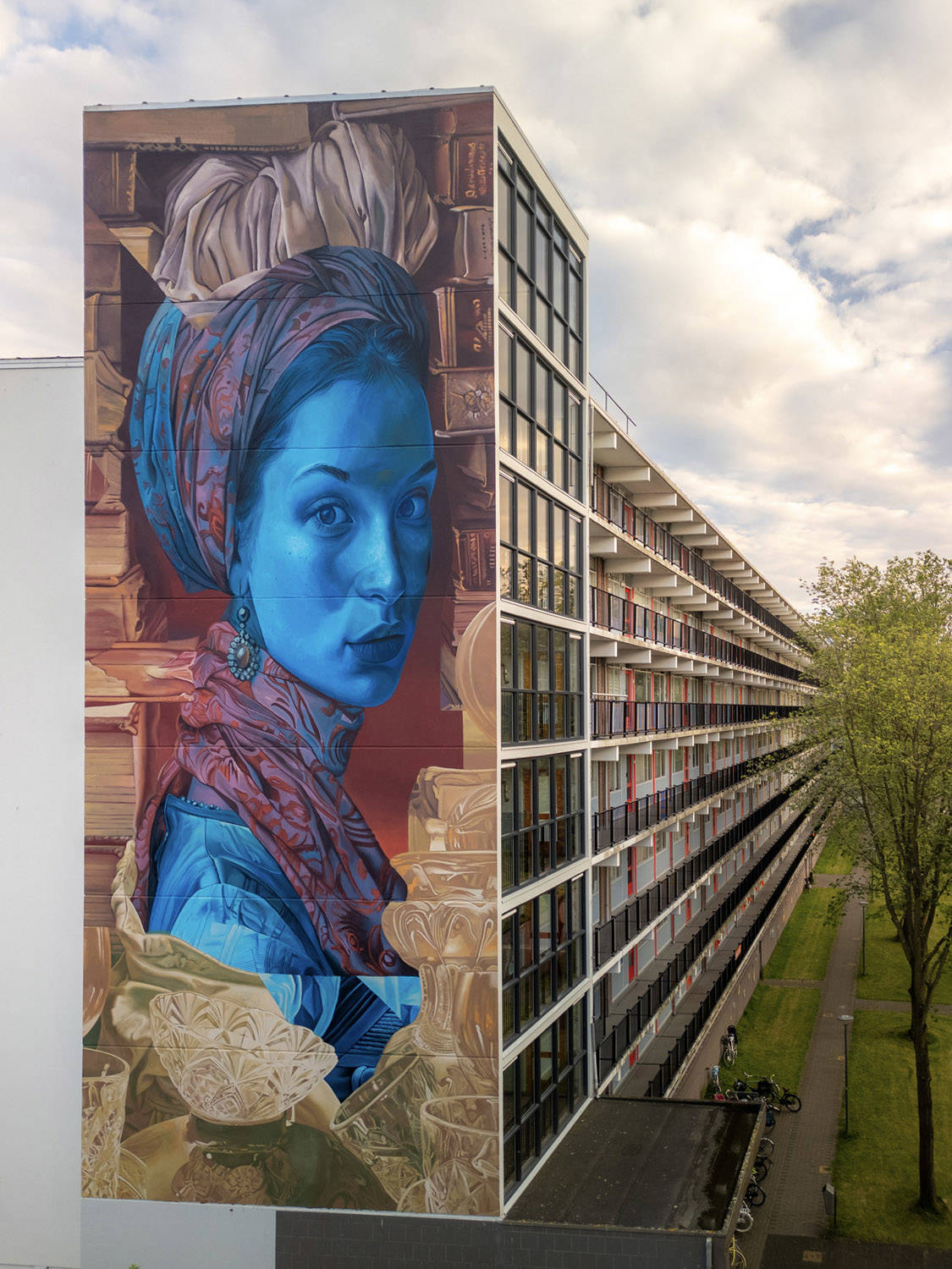 Telmomiel liet zich voor deze mural inspireren door het Stedelijk Museum Alkmaar. We zien het portret van een vrouw, omringd door kristal en boeken, aan de zijkant van een flatgebouw.