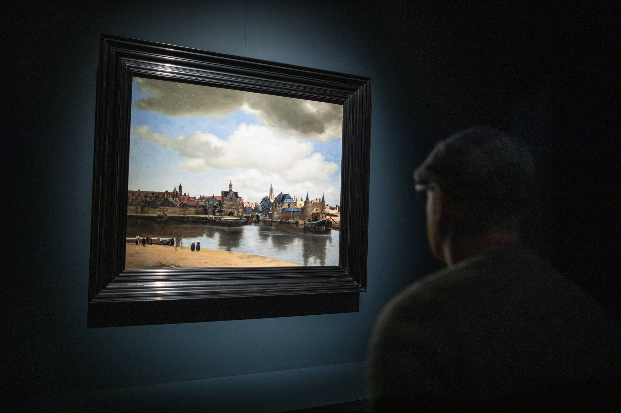 Een bezoeker kijkt in het donker naar Gezicht op Delft van Johannes Vermeer in het Mauritshuis.
