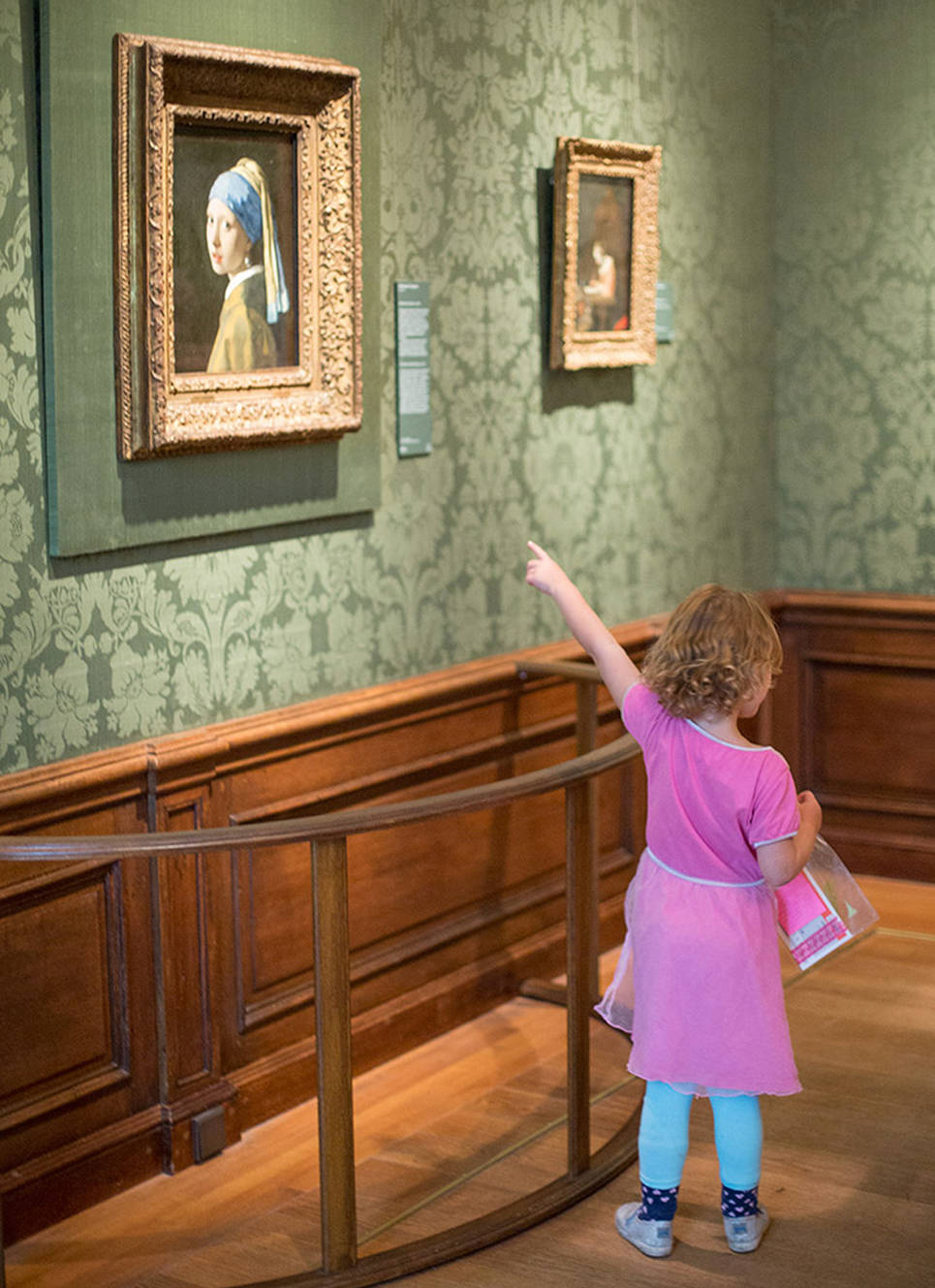 Een meisje in een roze jurkje wijst naar het schilderij 'Meisje met de Parel' van Johannes Vermeer