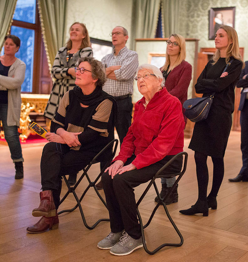 Een groep deelnemers aan 'Onvergetelijk' staan en zitten in een zaal van het Mauritshuis.