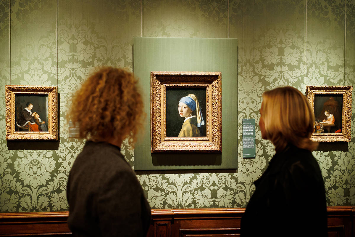 Twee bezoekers kijken vanaf een afstandje naar 'Meisje met de parel' van Johannes Vermeer in het Mauritshuis