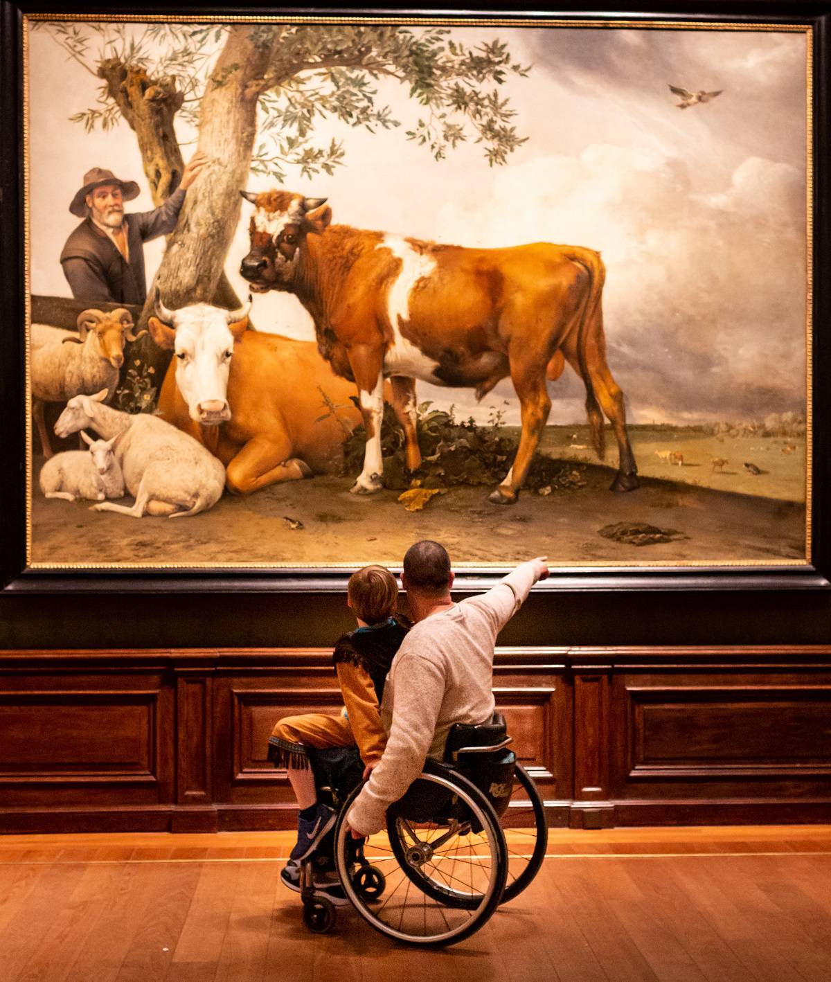 Een vader in een rolstoel wijst zijn kind een detail aan van het schilderij de Stier van Paulus Potter in het Mauritshuis.