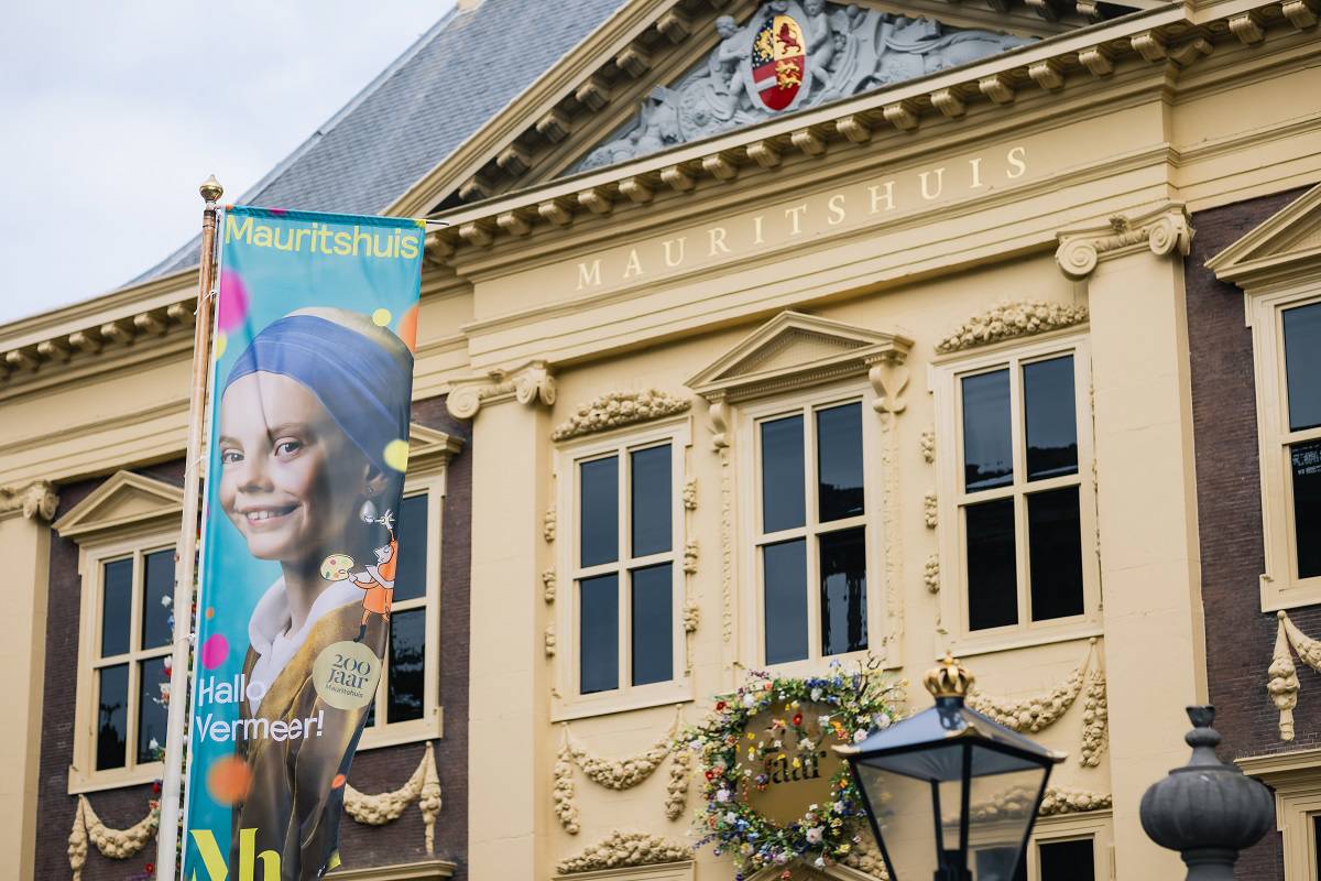 De gevel van het Mauritshuis met daarvoor een vlag met 'Hallo Vermeer!'