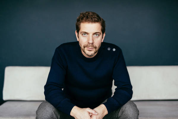 Een foto van Ramsey Nasr op de bank. Hij kijkt de camera in en heeft zijn handen in elkaar gevouwen.