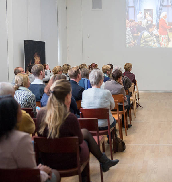 In de Nassauzaal van het Mauritshuis is een grote groep mensen bijeen gekomen voor een lezing.
