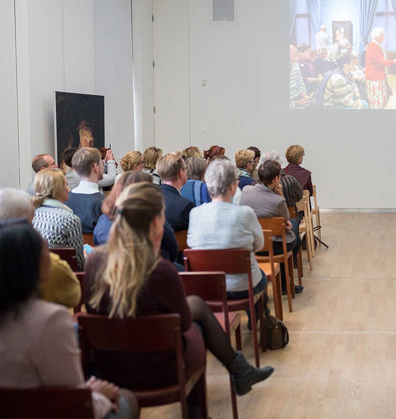 In de Nassauzaal van het Mauritshuis is een grote groep mensen bijeen gekomen voor een lezing.