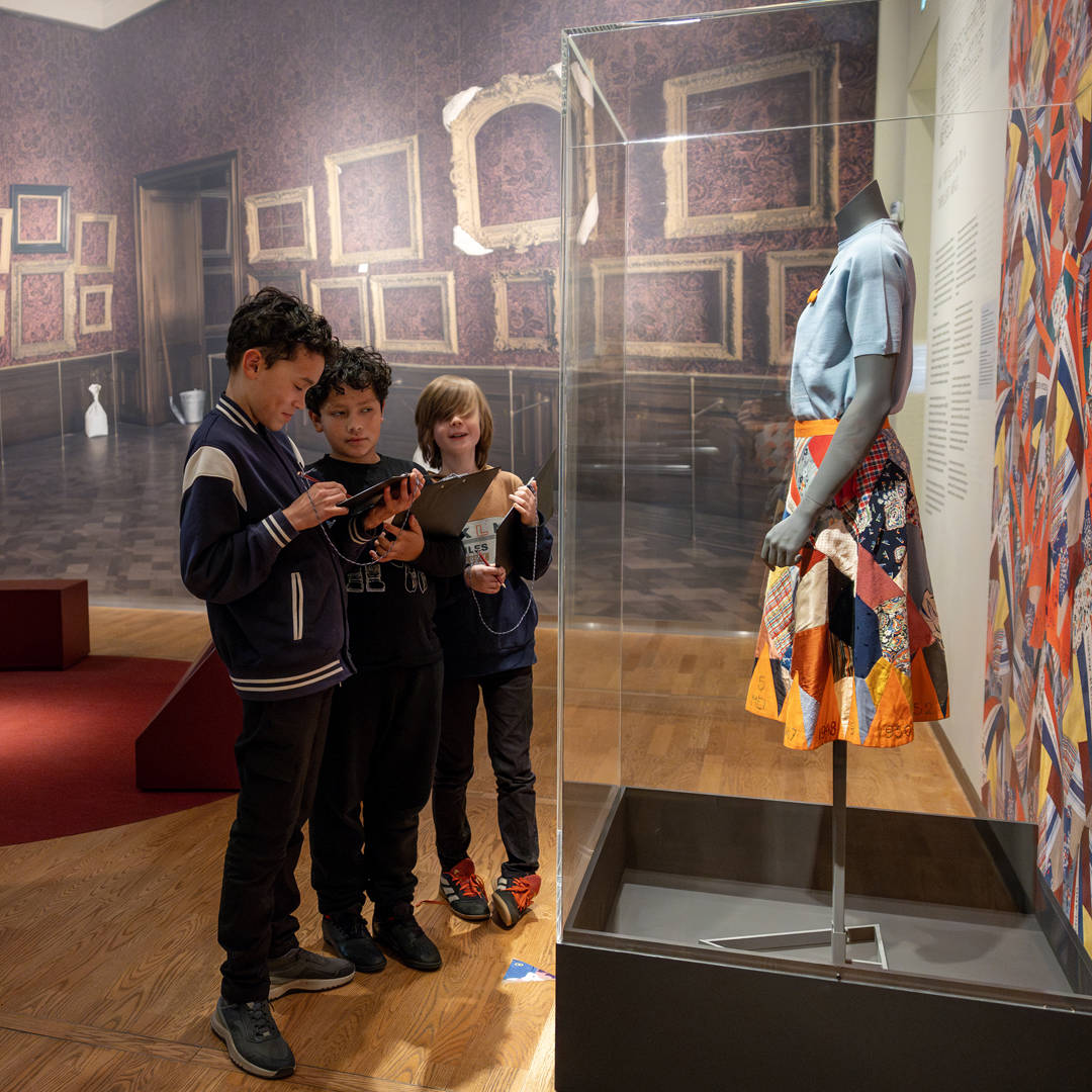 Kinderen maken met een logboek opdrachten bij de bevrijdingsrok in de tentoonstelling Huis in de Storm in het Mauritshuis.