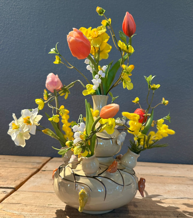 Een boeket van kleurrijke zijden bloemen staan in een tulpenvaas.