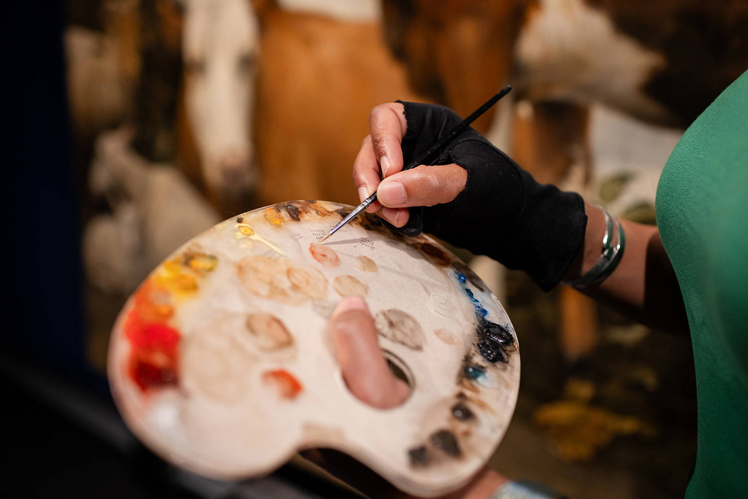 Een hand heeft een palet vast met allerlei kleuren verf.