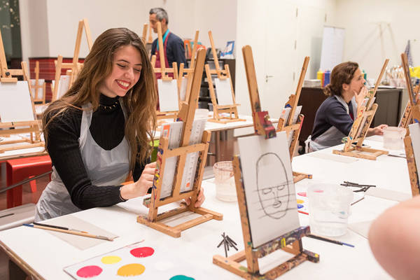 Een vrouw lacht terwijl zij schildert in de Kunstwerkplaats van het Mauritshuis.