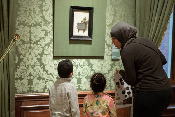 Een moeder kijkt met twee kinderen naar 'Het Puttertje' van Fabritius in het Mauritshuis.