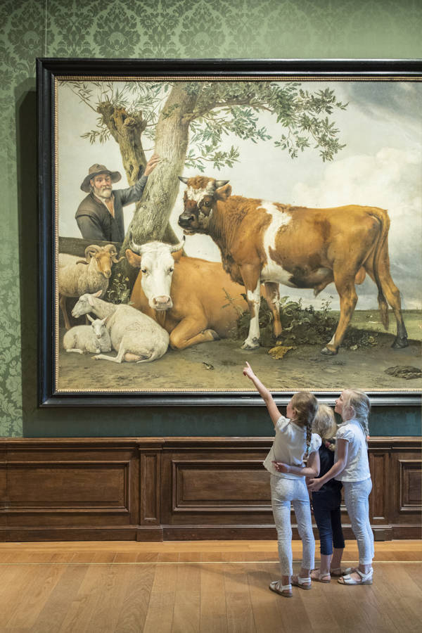 Drie kinderen staan en wijzen bij het beroemde schilderij 'De stier' van Paulus Potter.