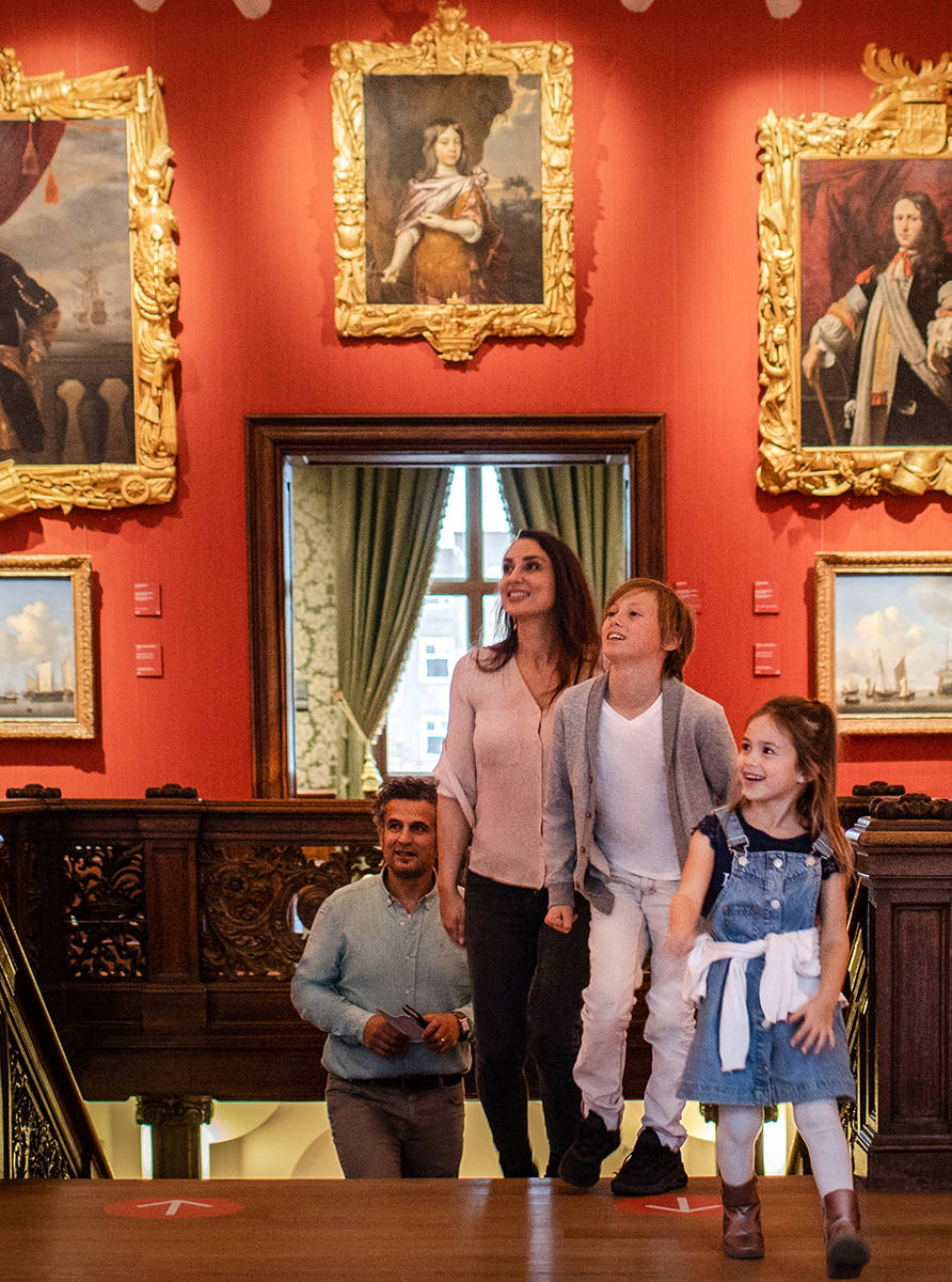 De Trapzaal van het Mauritshuis, een moeder, vader, zoon en dochter, beklimmen de trap en bekijken de schilderijen.