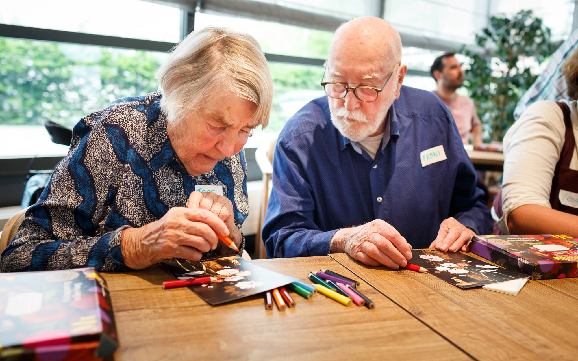 Twee oudere mensen doen met kleurpotloden een oefening met één van de schilderijen van het Mauritshuis.