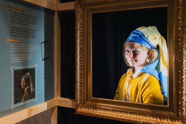 Een meisje verkleed als het Meisje met de Parel poseert in een gouden lijst.