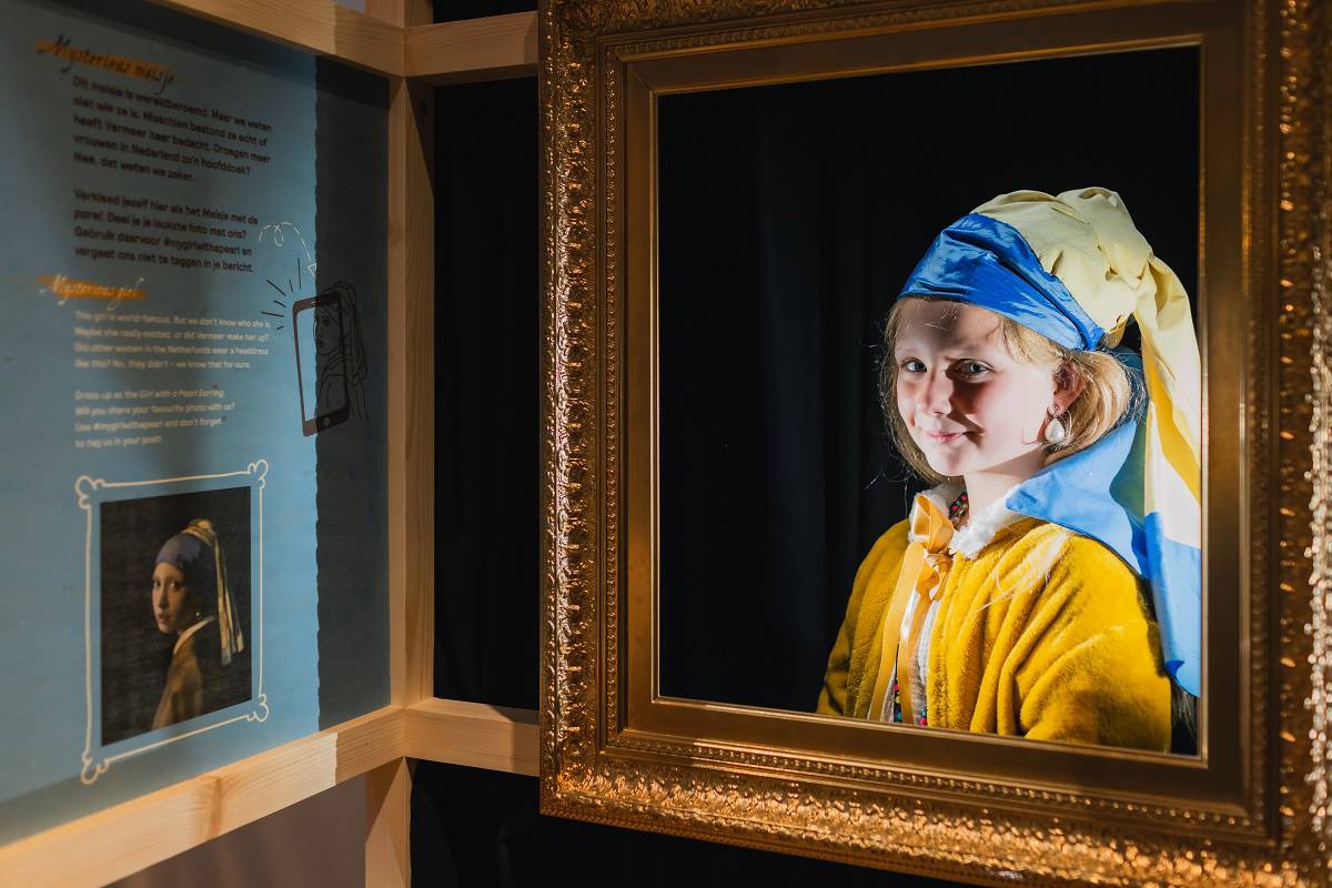 Een meisje verkleed als het Meisje met de Parel poseert in een gouden lijst.