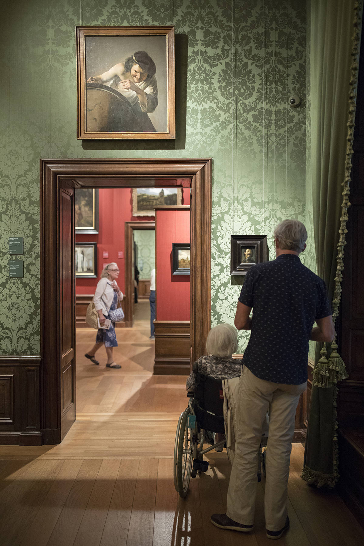 Een man en een vrouw in een rolstoel kijken naar de Lachende Man van Rembrandt in het Mauritshuis in Den Haag.